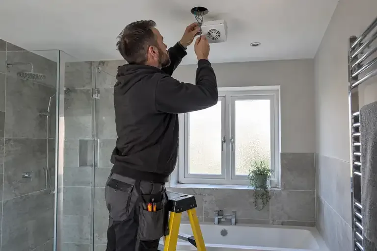 Electrician installing a ceiling extractor in a dry bathroom.