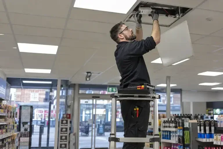 Electrician repairing a ceiling light panel in a shop
